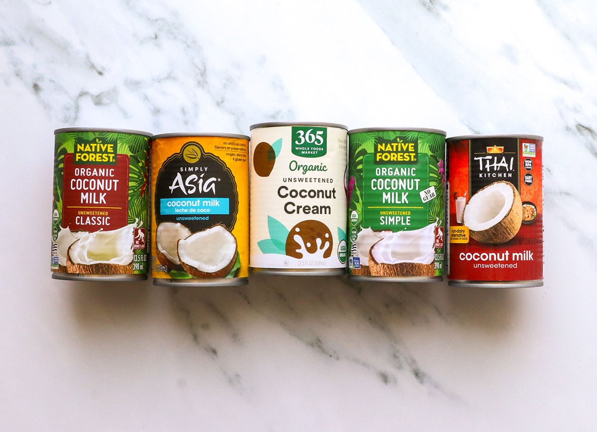 5 different kinds of canned coconut milk on a marble surface.