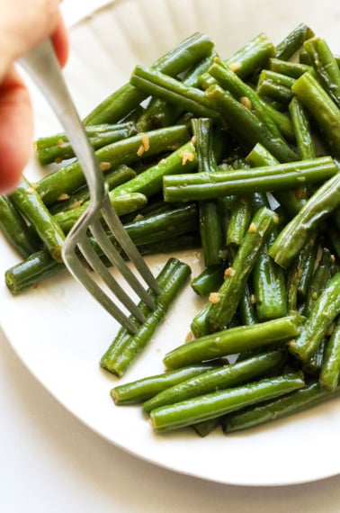 sauteed green beans on a white plate with a fork grabbing one.
