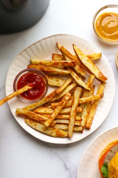 french fry dipped into ketchup on a white plate.