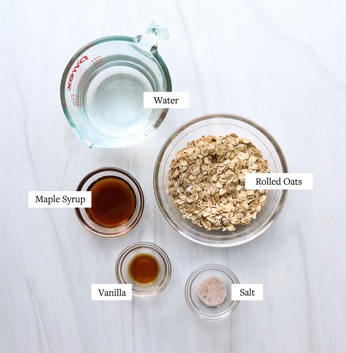 oat milk ingredients labeled in glass bowls on a white surface.