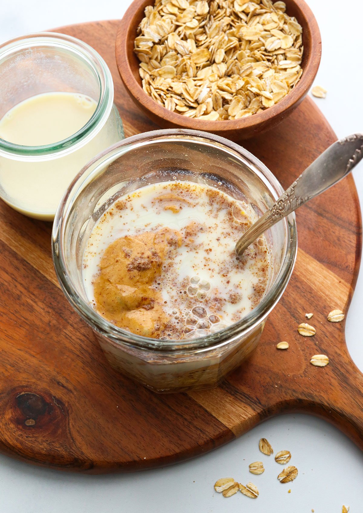overnight oats ingredients added to a glass jar with a spoon.