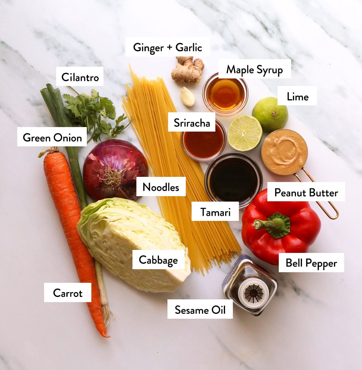 pasta, veggies, and peanut sauce ingredients labeled on a white surface.