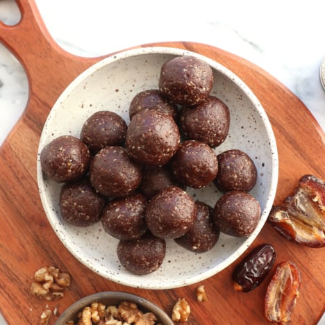 chocolate date balls in a white bowl near walnuts and dates.