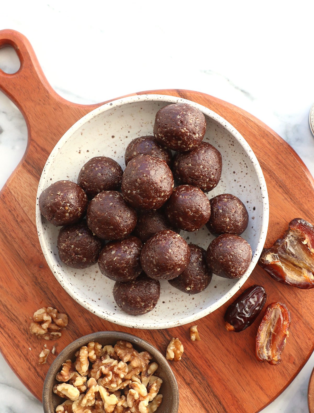 chocolate date balls in a white bowl near walnuts and dates. 
