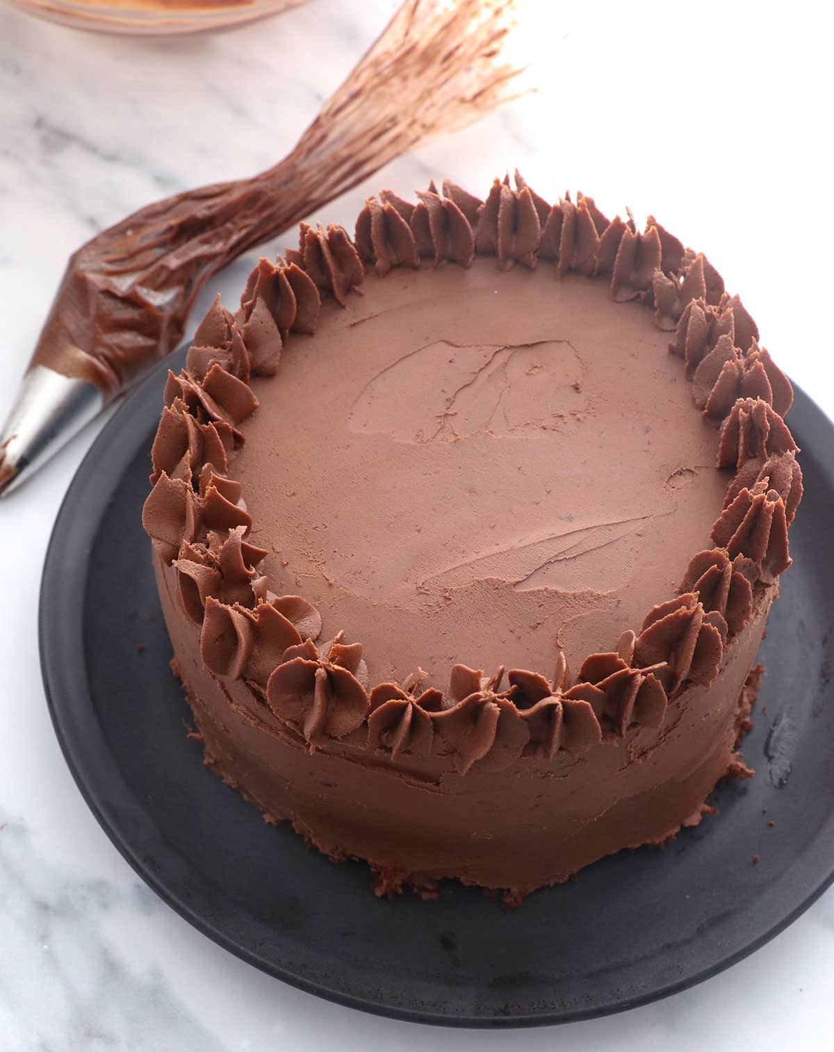 almond flour cake topped with chocolate frosting from a piping bag.