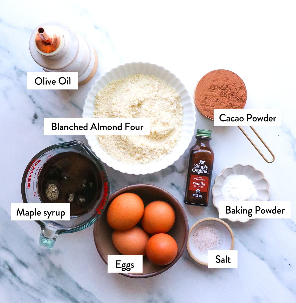 bowl of almond flour, eggs, baking powder, salt, and maple syrup on a marble surface.
