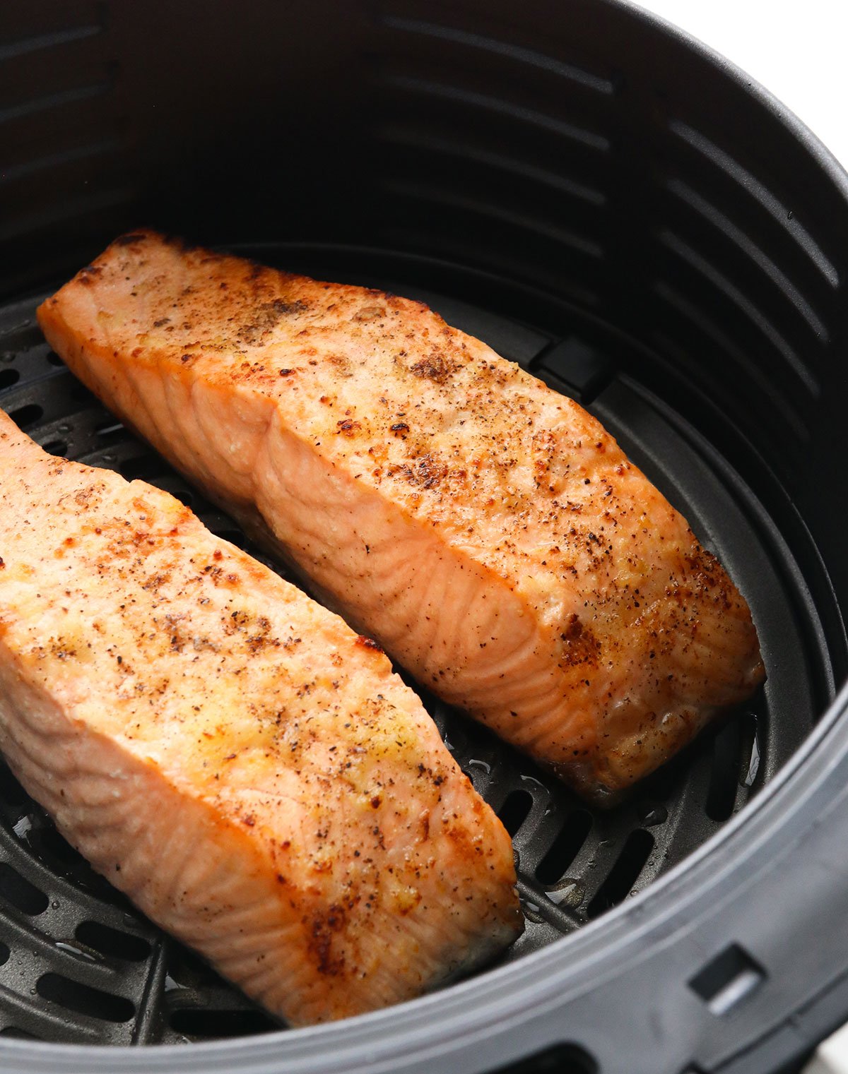 two salmon fillets cooked in a black air fryer basket.