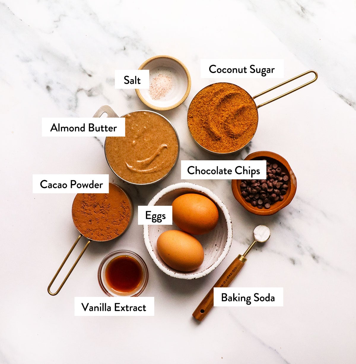almond butter, coconut sugar, eggs, cacao powder, and vanilla labeled on a white surface.