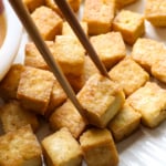 baked tofu pieces on a white plate with chopsticks. - 8