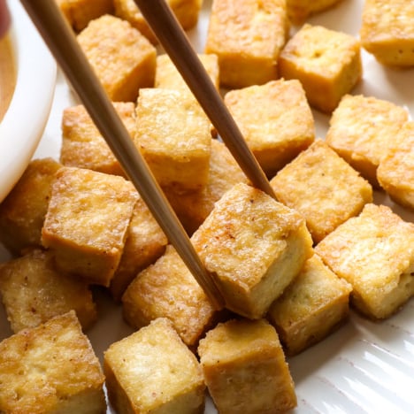 baked tofu pieces on a white plate with chopsticks.