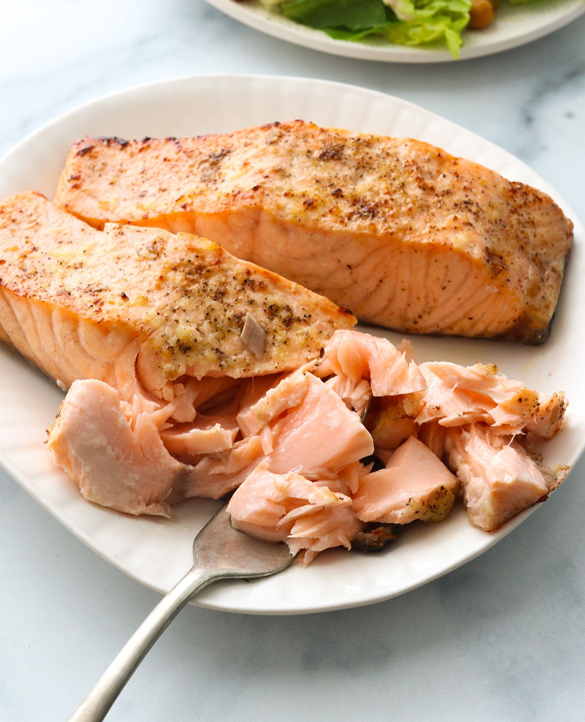 air fryer salmon flaked with a fork on a white plate.
