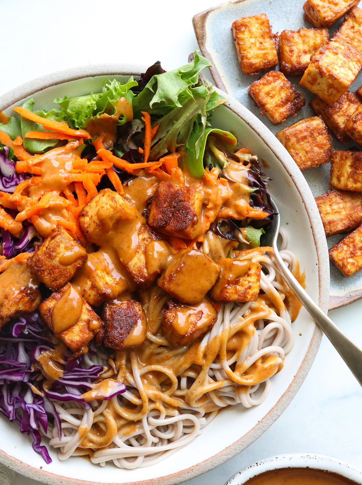 peanut sauce drizzled over a noodle bowl with baked tofu and red cabbage.