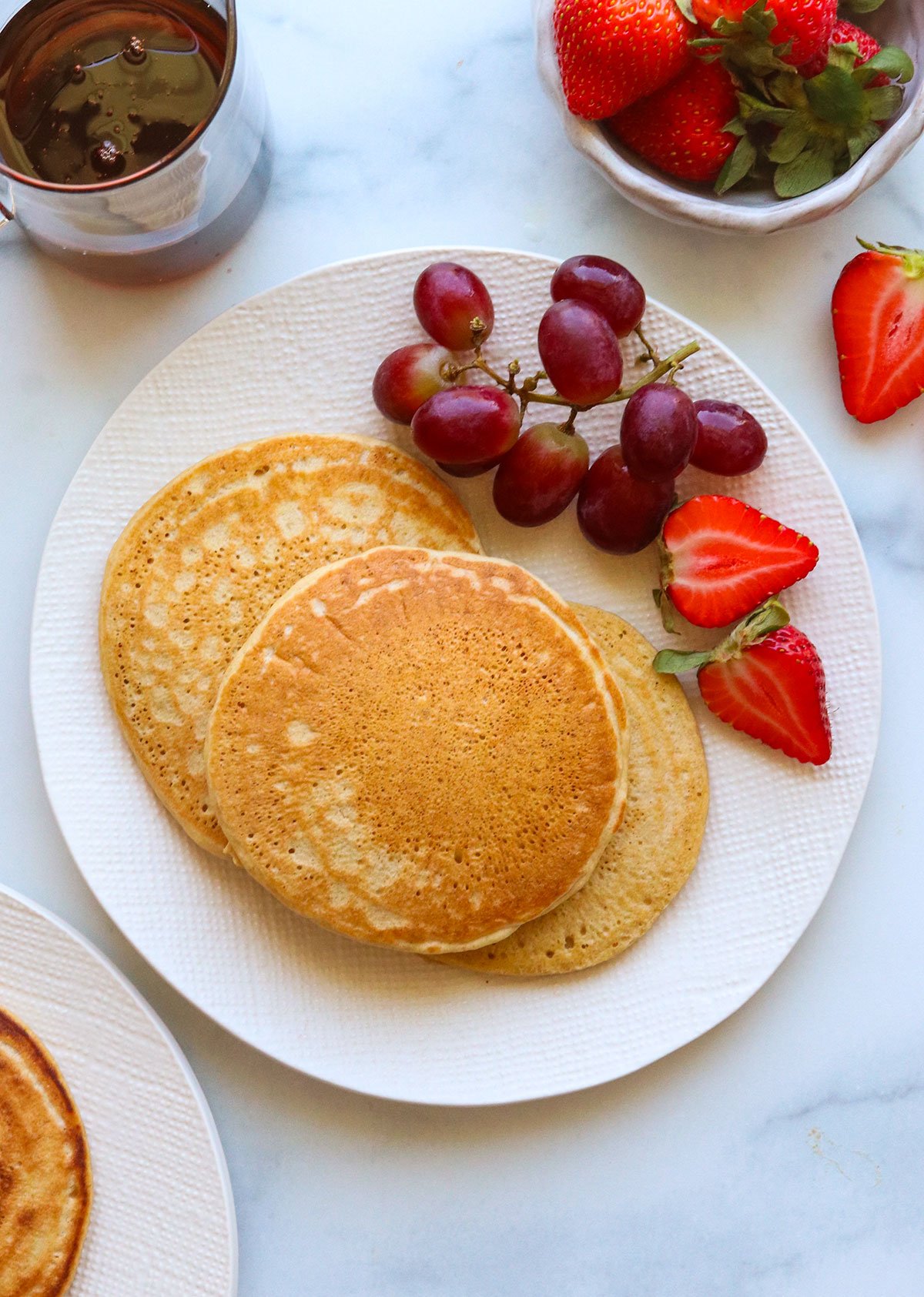 three oat flour pancakes served with fruit on a white plate.