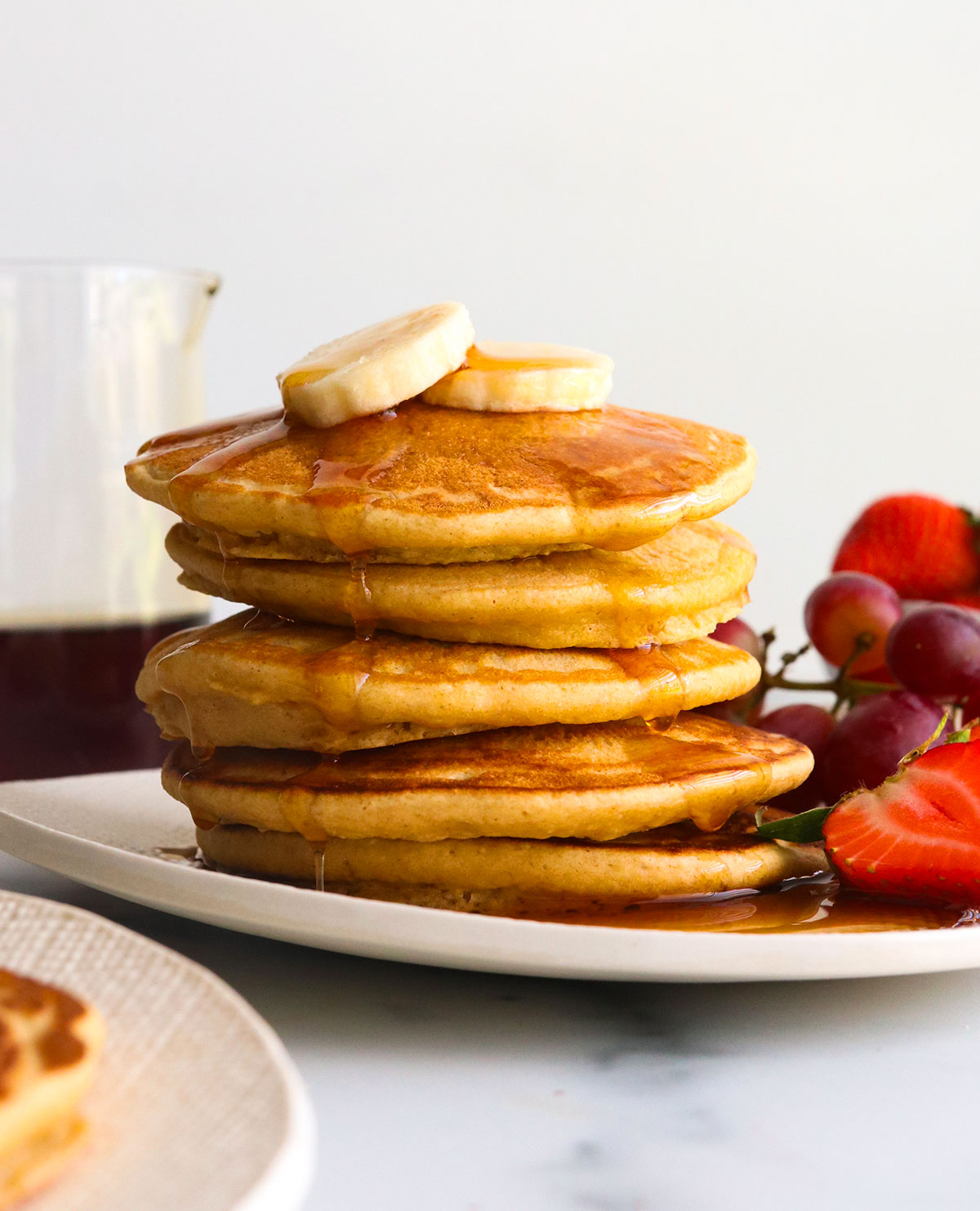 oat flour pancakes stacked on a white plate with syrup.