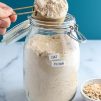 oat flour scooped from jar with blue background