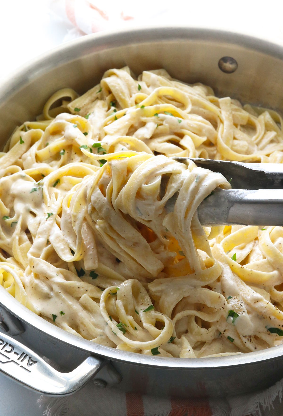 alfredo sauce tossed with metal tongs in a deep skillet.