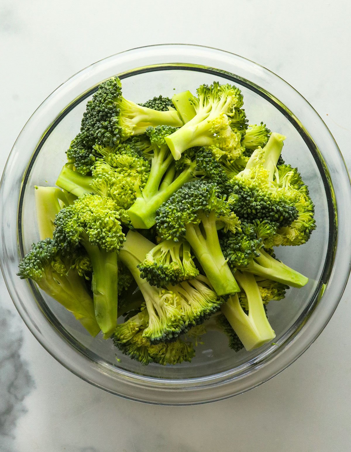 raw broccoli florets in a glass bowl.