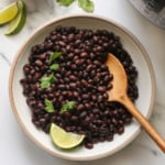 Black beans and wooden spoon and pressure cooker in a white bowl.