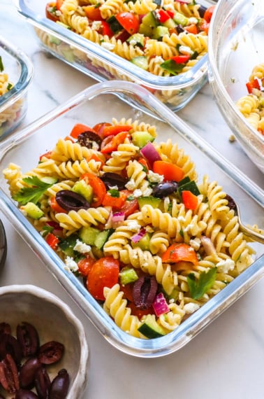 greek pasta salad in a glass jar with a fork.