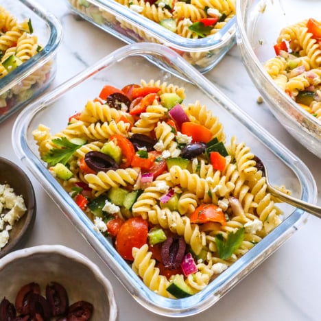 greek pasta salad in a glass jar with a fork.