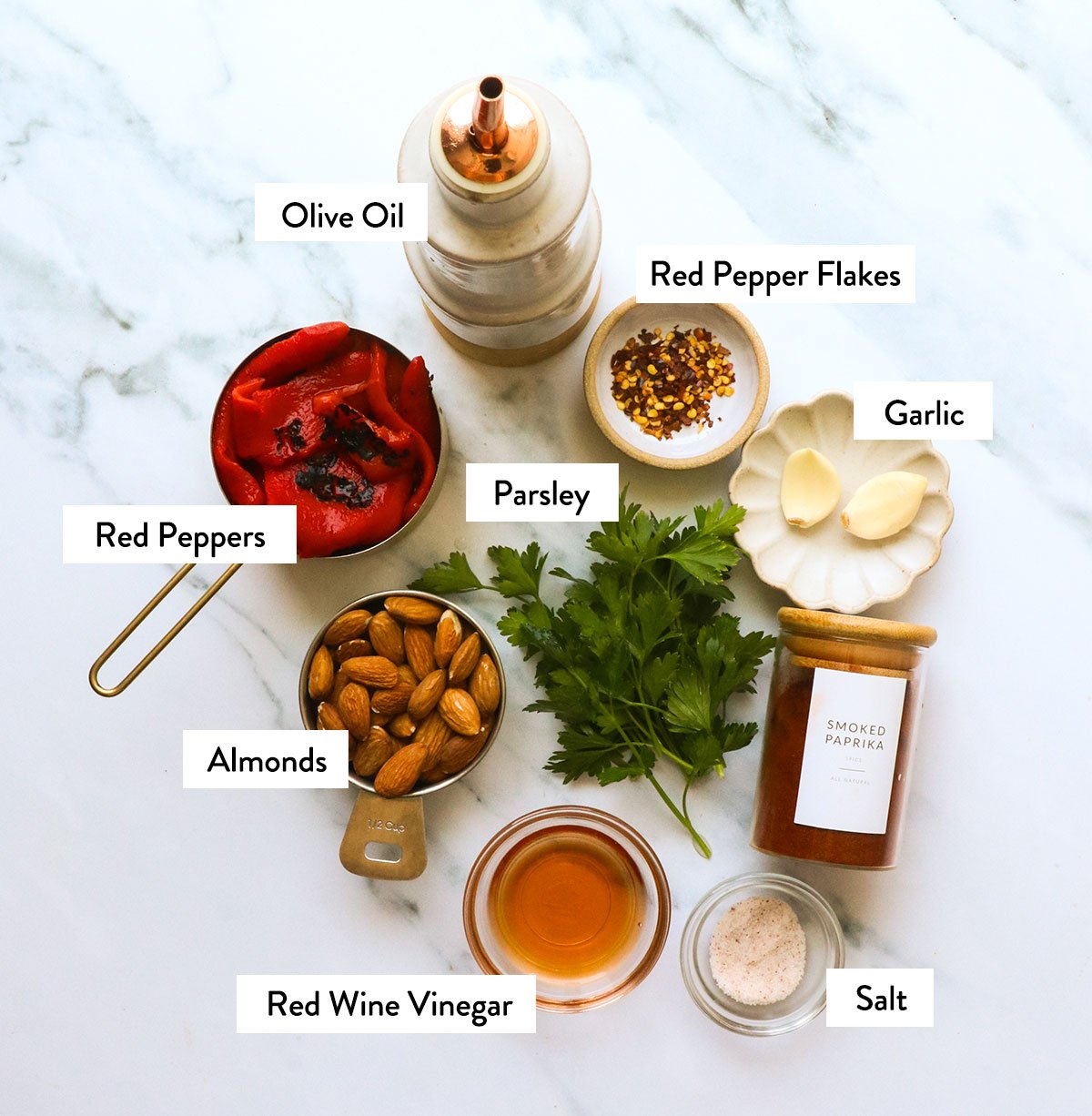 roasted red peppers, almonds, parsley, garlic, and spices labeled on a white surface.