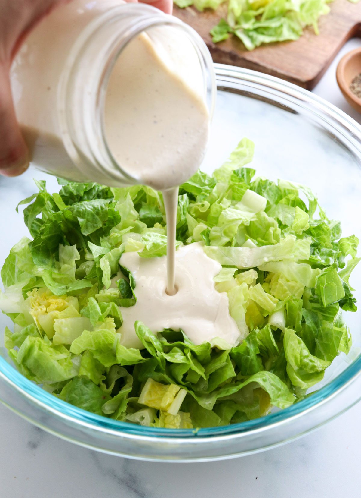 vegan caesar dressing poured on bowl of lettuce