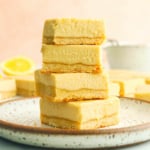 vegan lemon bars stacked on a white plate with pink background.
