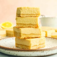 vegan lemon bars stacked on a white plate with pink background.