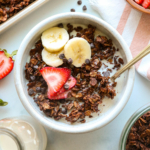 A bowl of chocolate granola topped with fresh fruit and mini chocolate chips.