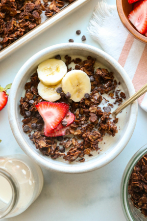 A bowl of chocolate granola topped with fresh fruit and mini chocolate chips.