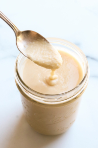 homemade coconut butter dripping off of a spoon into a jar.