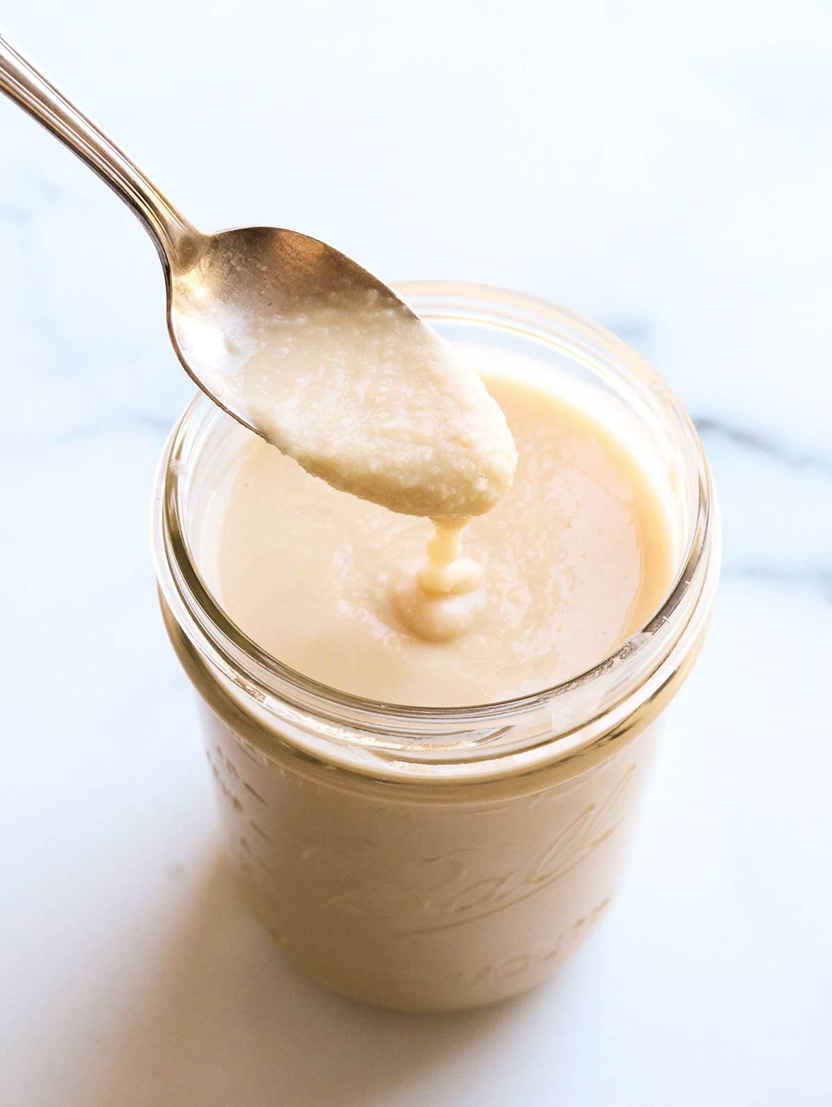 homemade coconut butter dripping off of a spoon into a jar.