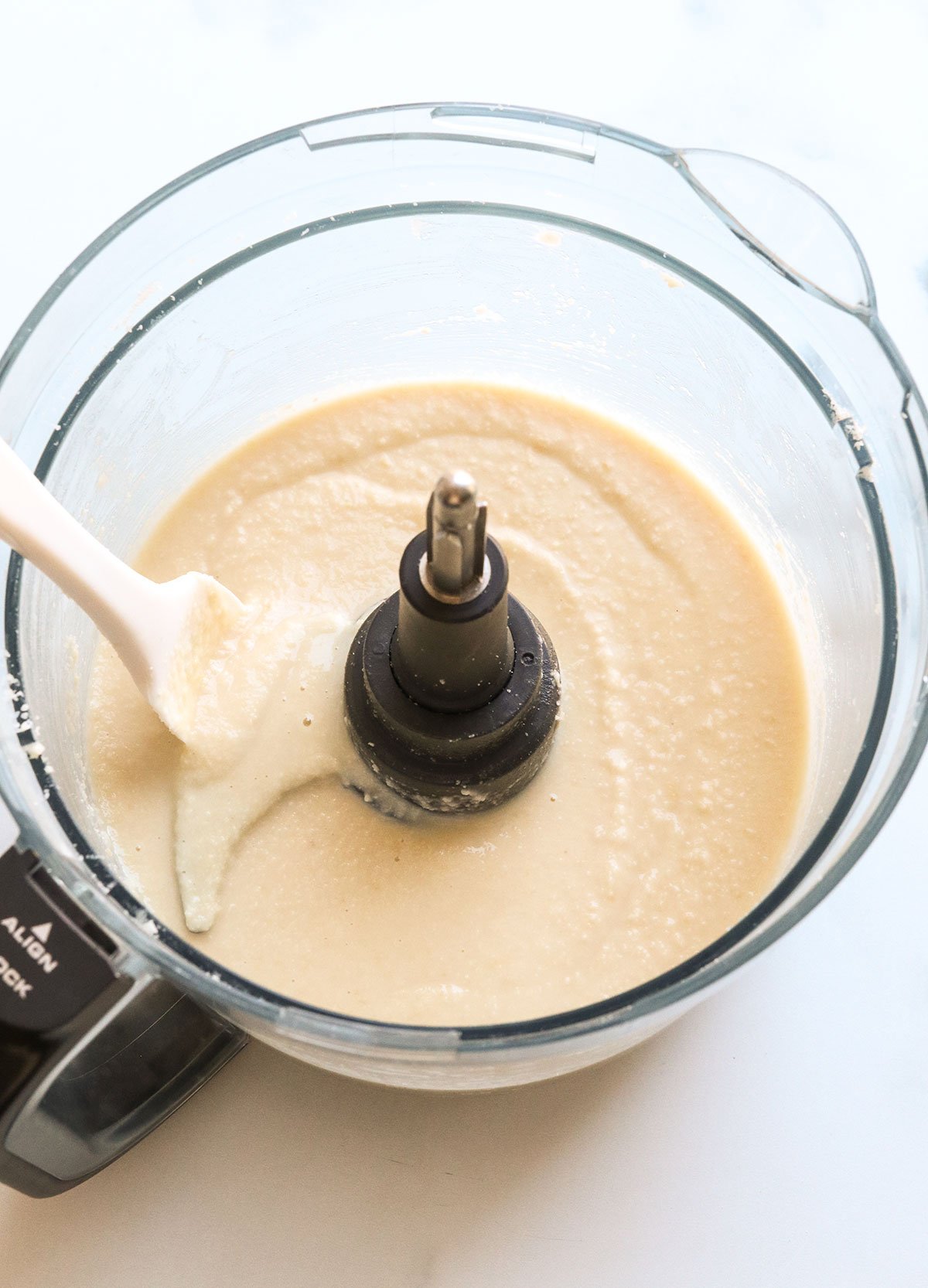 Coconut butter in a food processor with a spatula.