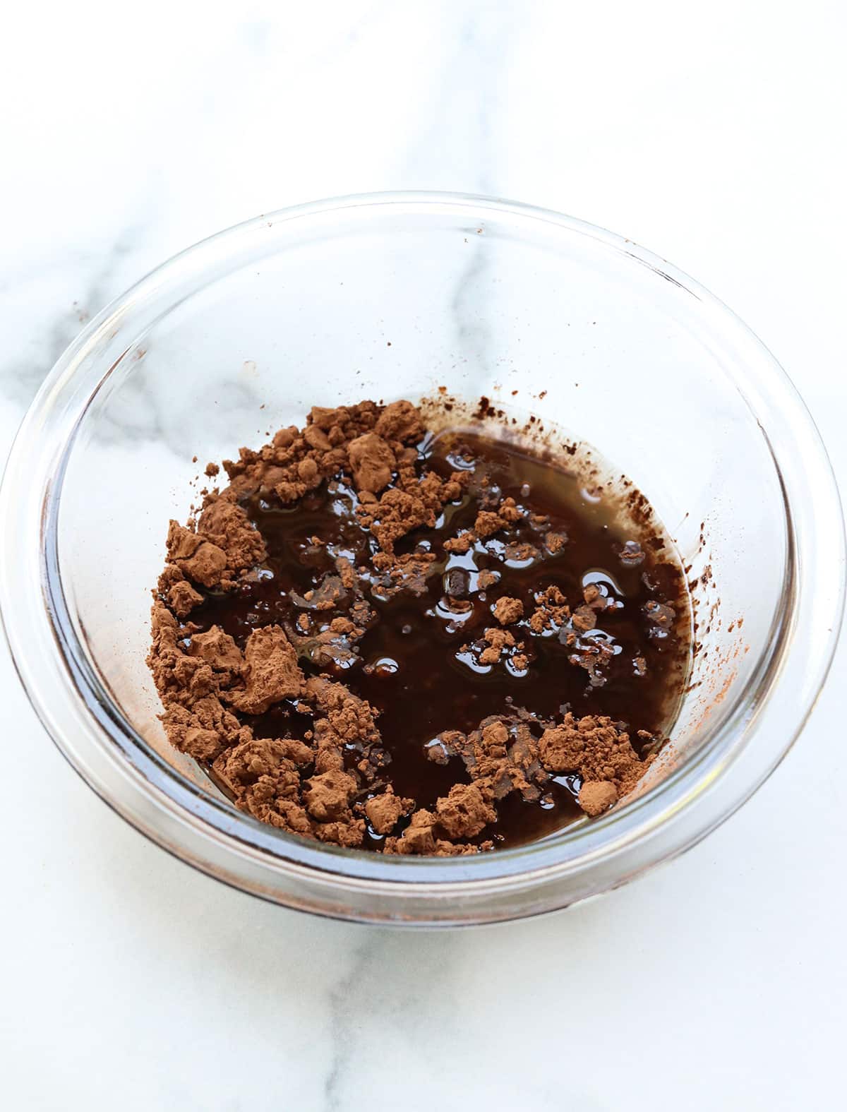 cocoa powder mixed with maple syrup and coconut oil in a glass bowl.