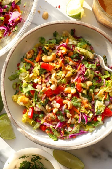 thai salad topped with peanut dressing in a white bowl with a fork.