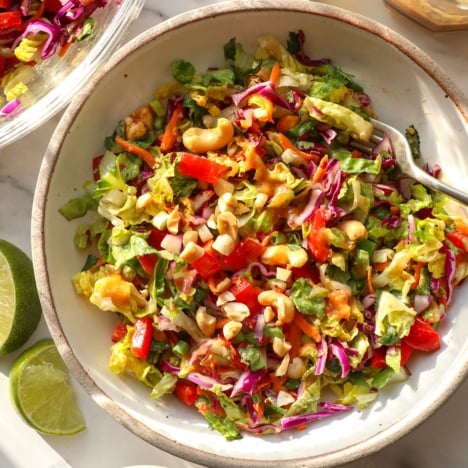 thai salad topped with peanut dressing in a white bowl with a fork.