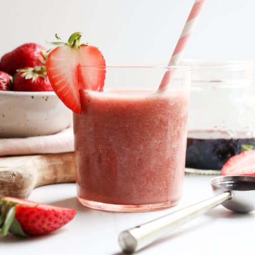 elderberry smoothie in glass with pink straw and strawberry