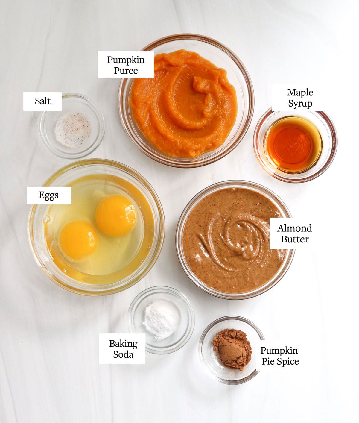 ingredients for pumpkin pancakes in glass bowls on white surface