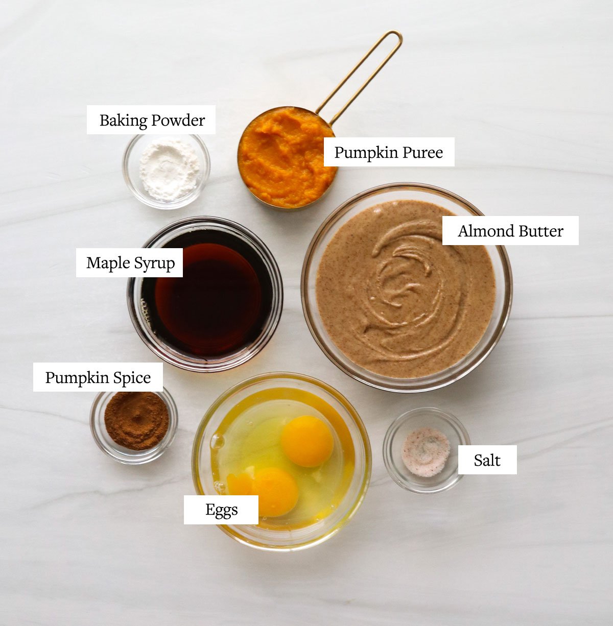 Paleo pumpkin muffin ingredients labeled in glass bowls.