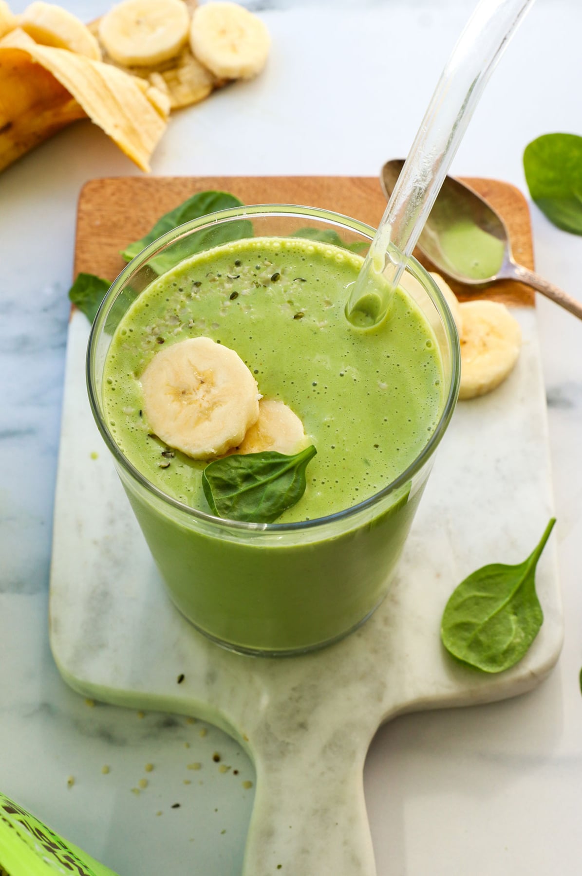 spinach banana smoothie served in a glass with a straw. 