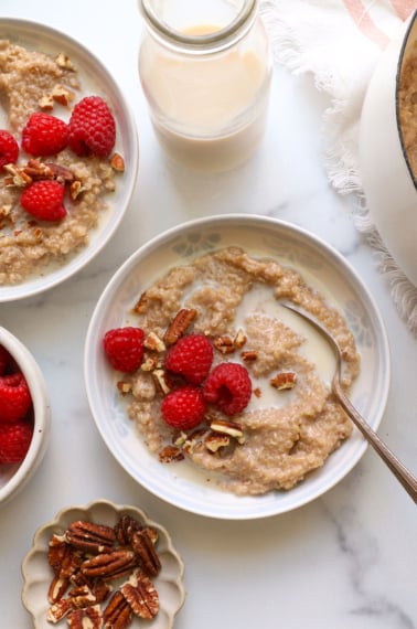 two bowls of quinoa porridge topped with raspberries and milk.