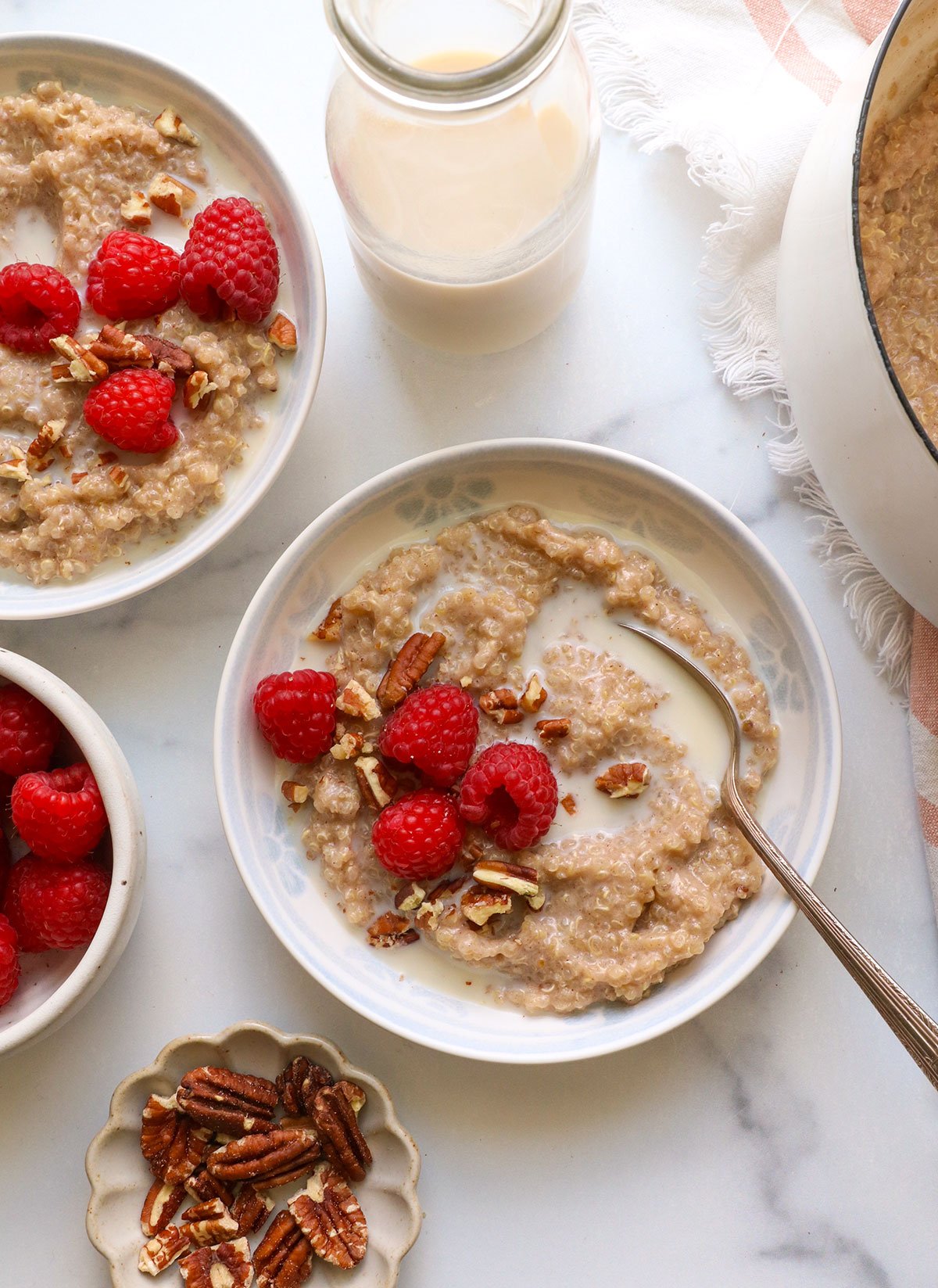 two bowls of quinoa porridge topped with raspberries and milk.
