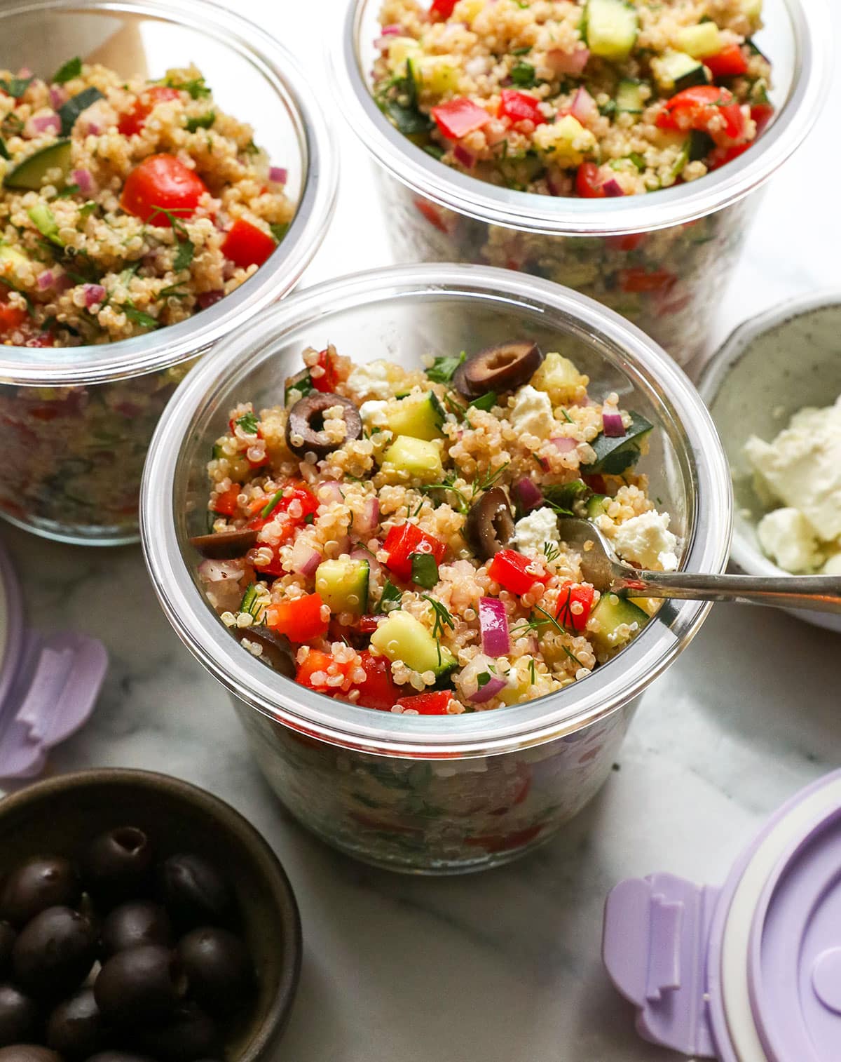 quinoa salad in individual meal prep jars with black olives and feta on top.