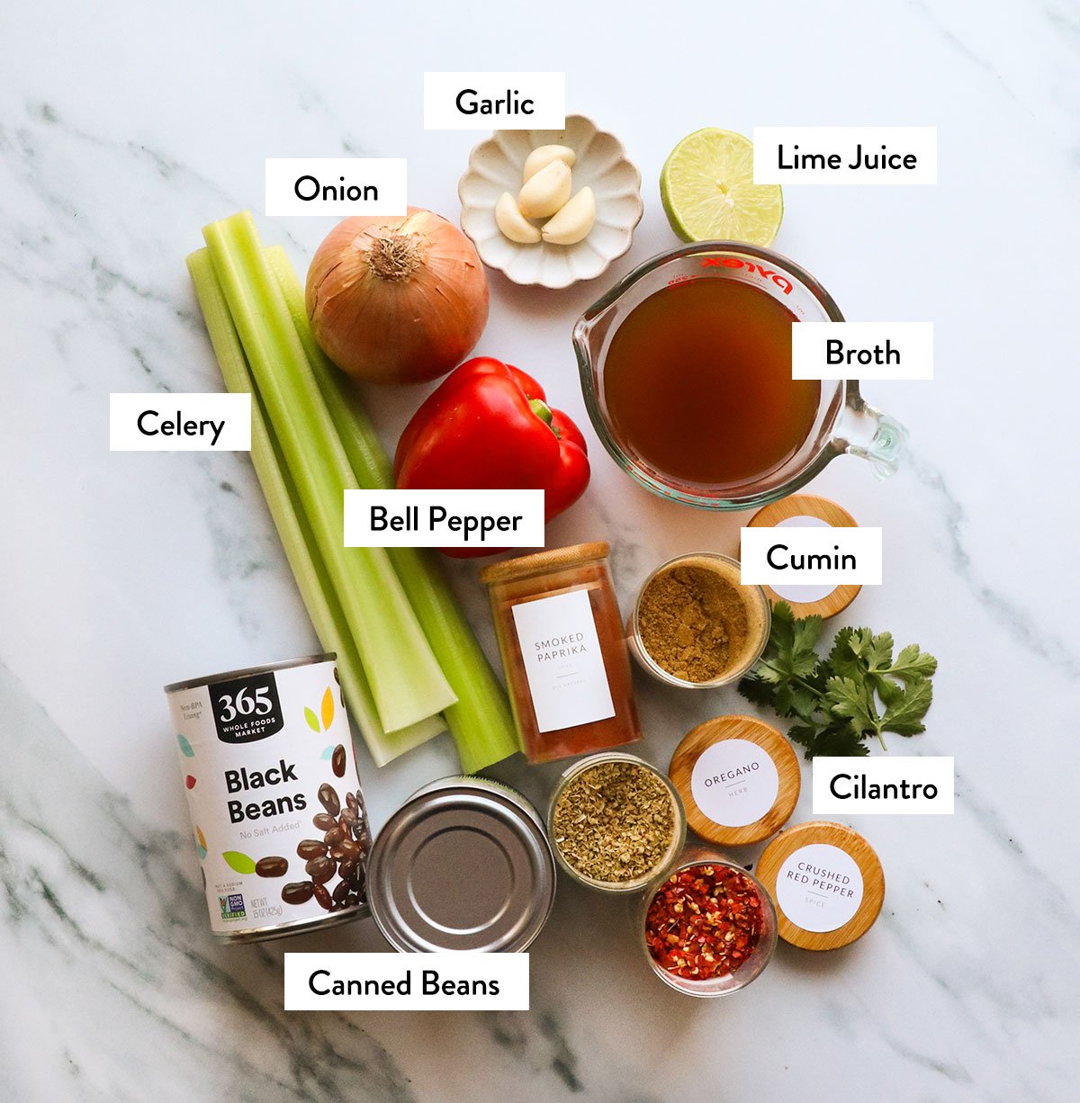 canned beans, celery, bell pepper, onion, and spices labeled on a white surface. 