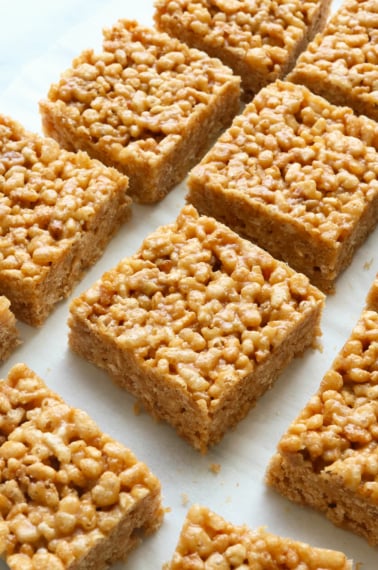 peanut butter rice crispy treats cut into squares on white parchment.
