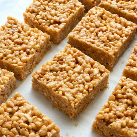 peanut butter rice crispy treats cut into squares on white parchment.