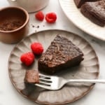 flourless chocolate cake served on a dark plate with raspberries.