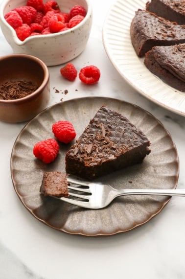 flourless chocolate cake served on a dark plate with raspberries.