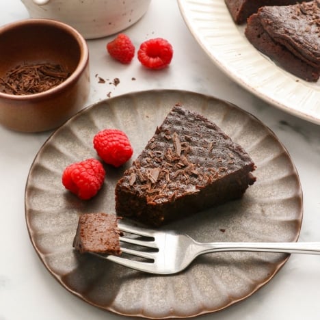 flourless chocolate cake served on a dark plate with raspberries.