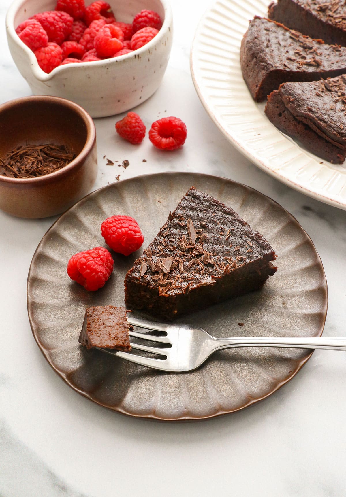 flourless chocolate cake served on a dark plate with raspberries.